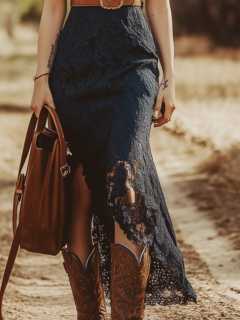 Woman in navy lace midi dress with cowboy boots, brown belt, and leather handbag, outdoor rustic setting